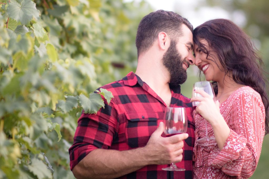 man and woman holding wine glasses touching foreheads in vineyard