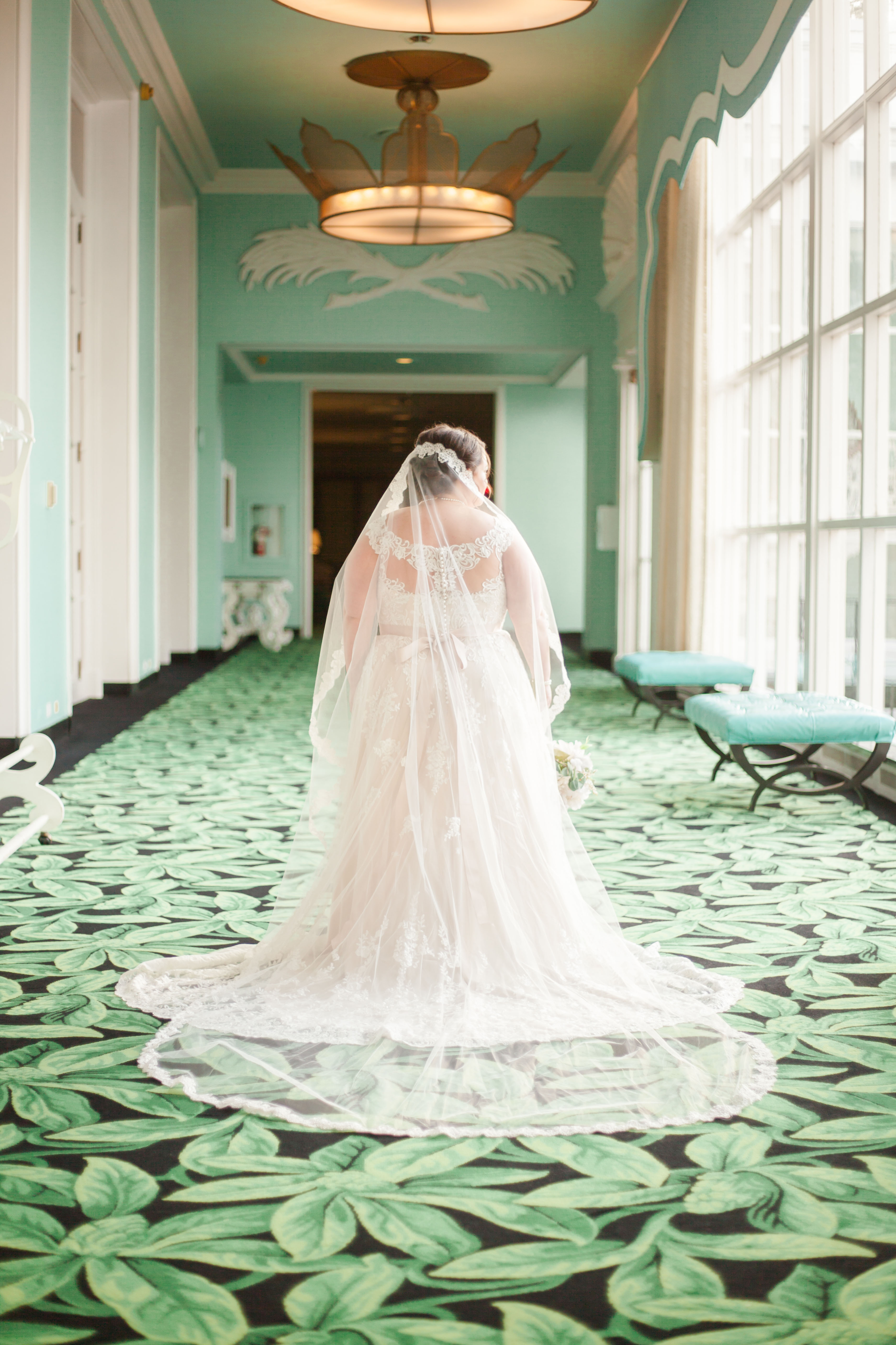 bride in gown and long veil standing on green floral carpet at greenbrier