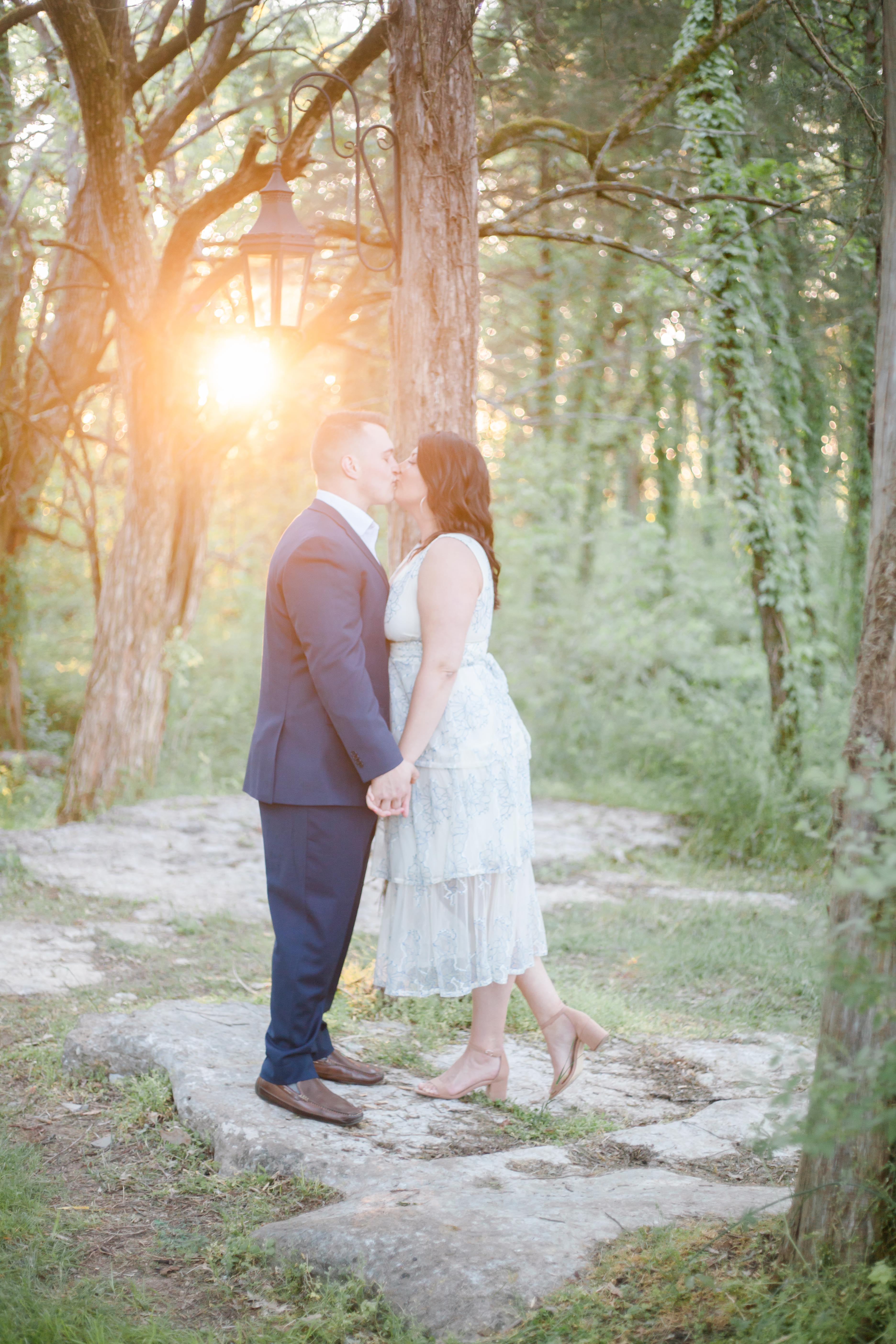 woman in white dress kissing guy in navy suit in woods