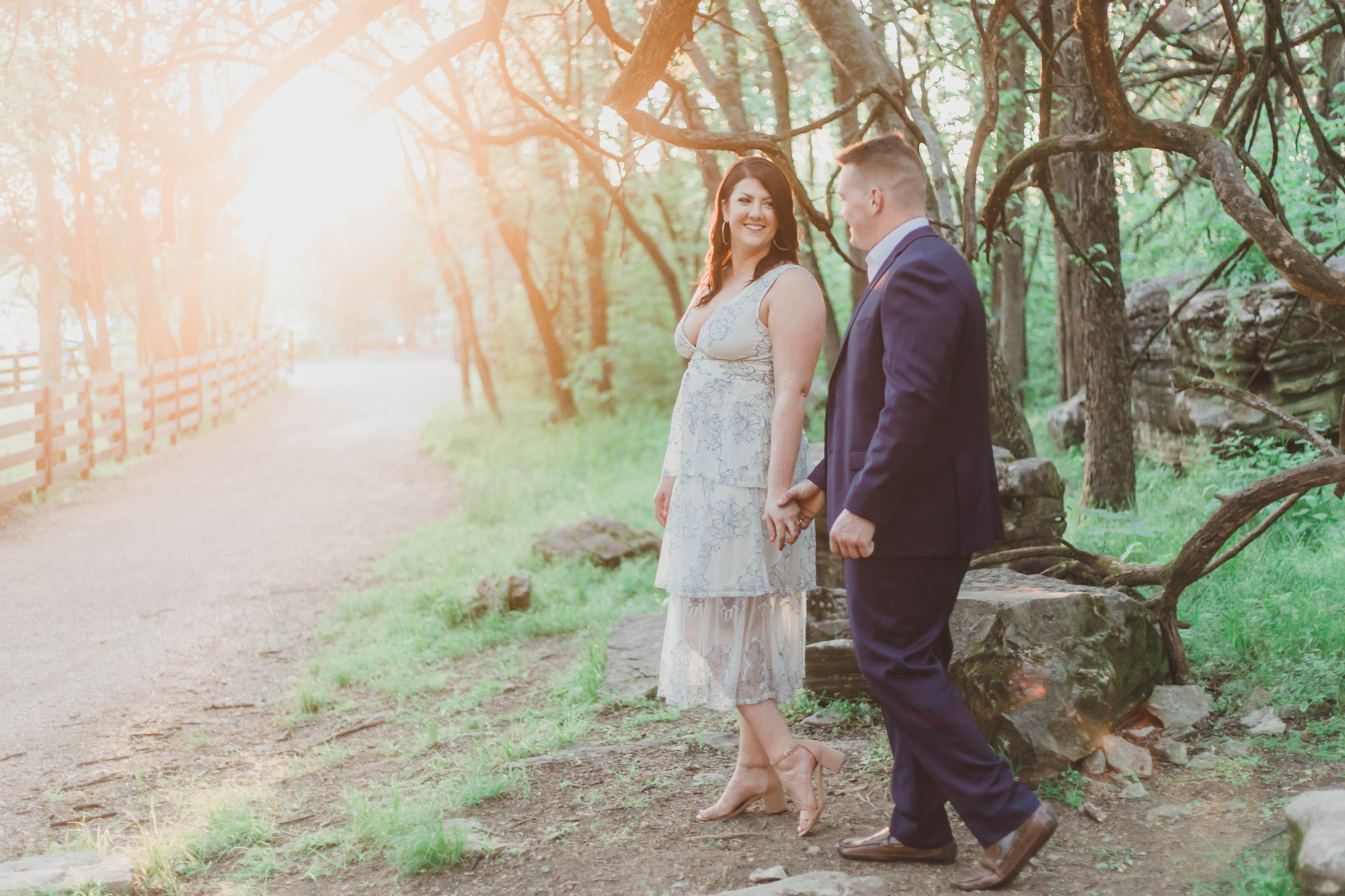 girl in white dress and guy in navy suit walking in woods