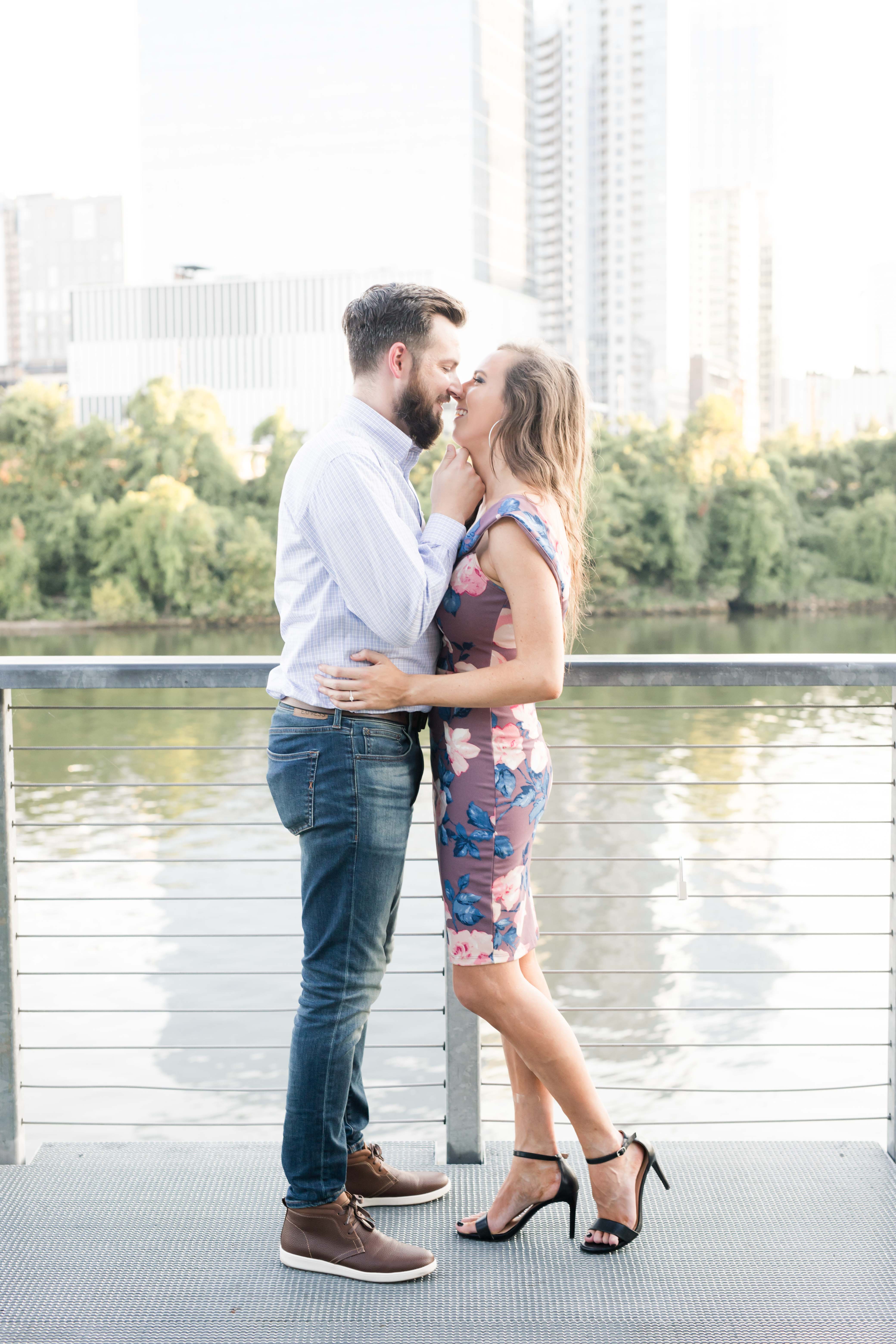 guy in button down brings girl in purple floral dress in for kiss by river