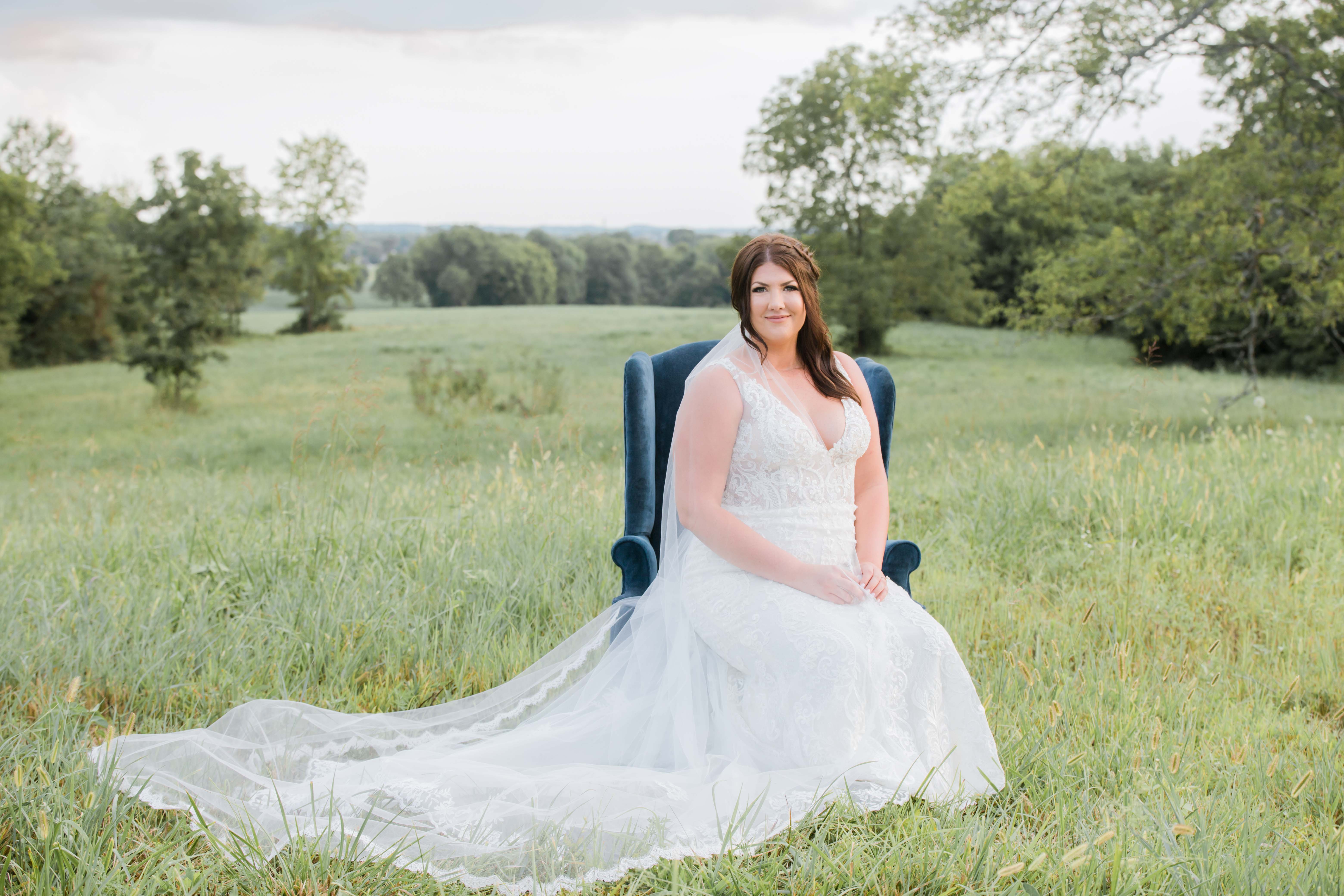 bride sitting in field in navy velvet chair