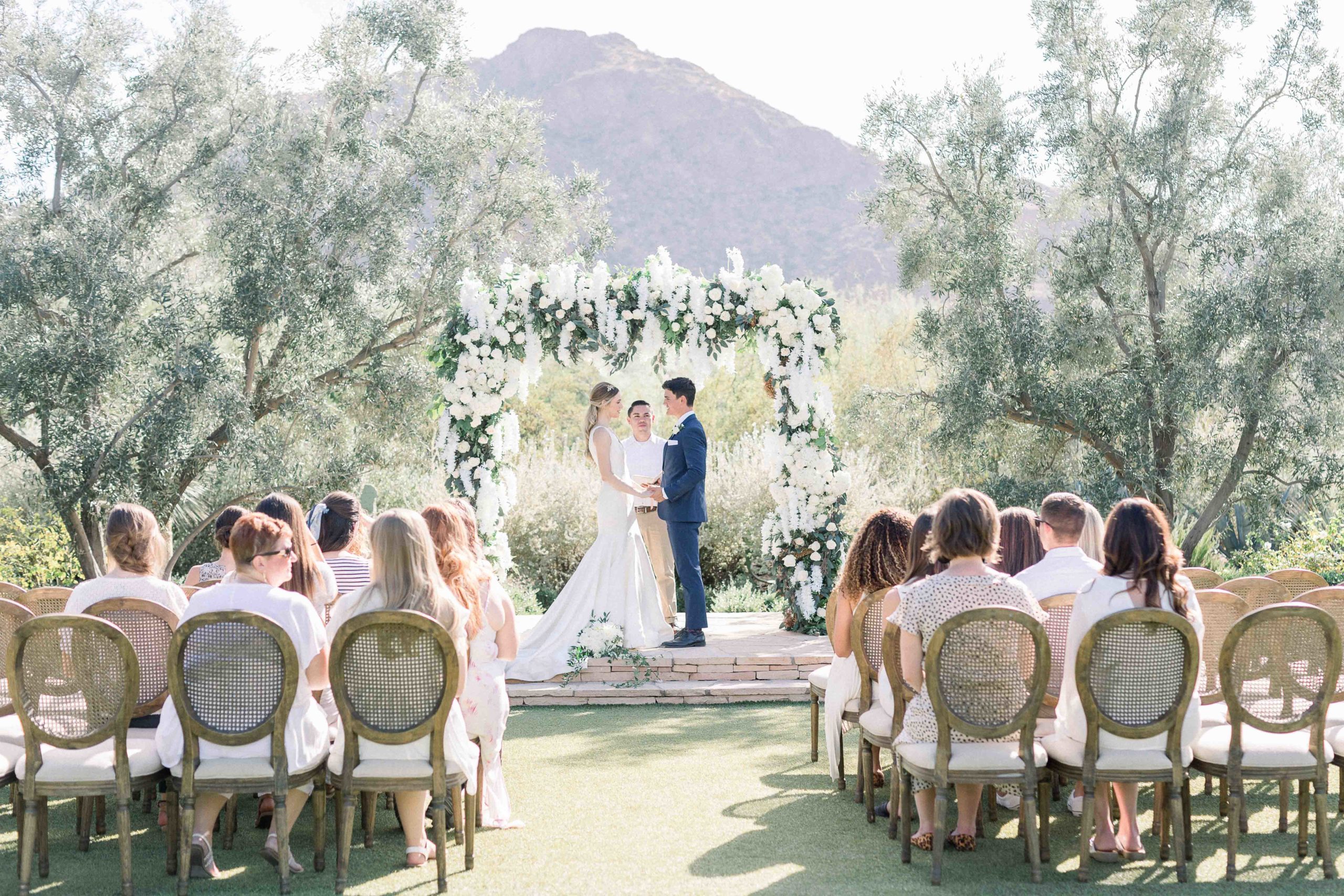 bride and groom under floral arch in arizona mountain background