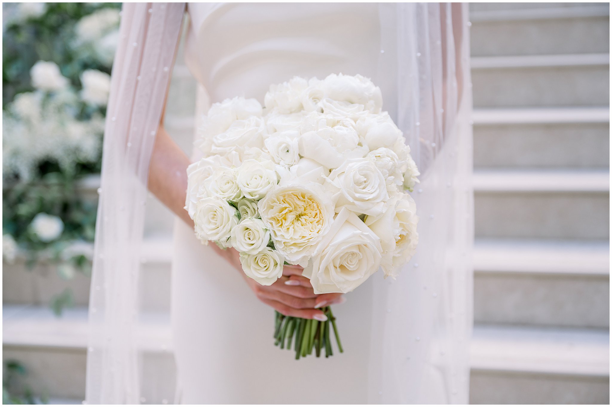 white bouquet of roses held by bride in white gown and veil